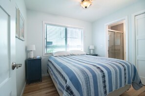 Een slaapkamer met een bed, een raam, een deur en een nachtkastje met een lamp.
