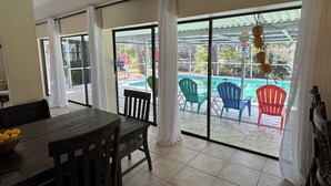 A room with a dining table and chairs, large sliding glass doors leading to a pool area with colorful chairs. - A little piece of heaven on the river (Port St Lucie)