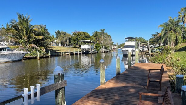A wooden dock with a bench, a calm water body, and boats docked in the background. - A little piece of heaven on the river (Port St Lucie)