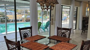 A dining area with a glass table surrounded by wicker chairs, a chandelier, and a view of a pool and outdoor seating. - A little piece of heaven on the river (Port St Lucie)