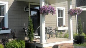 Une maison avec un porche couvert, des plantes en pot et des jardinières suspendues.