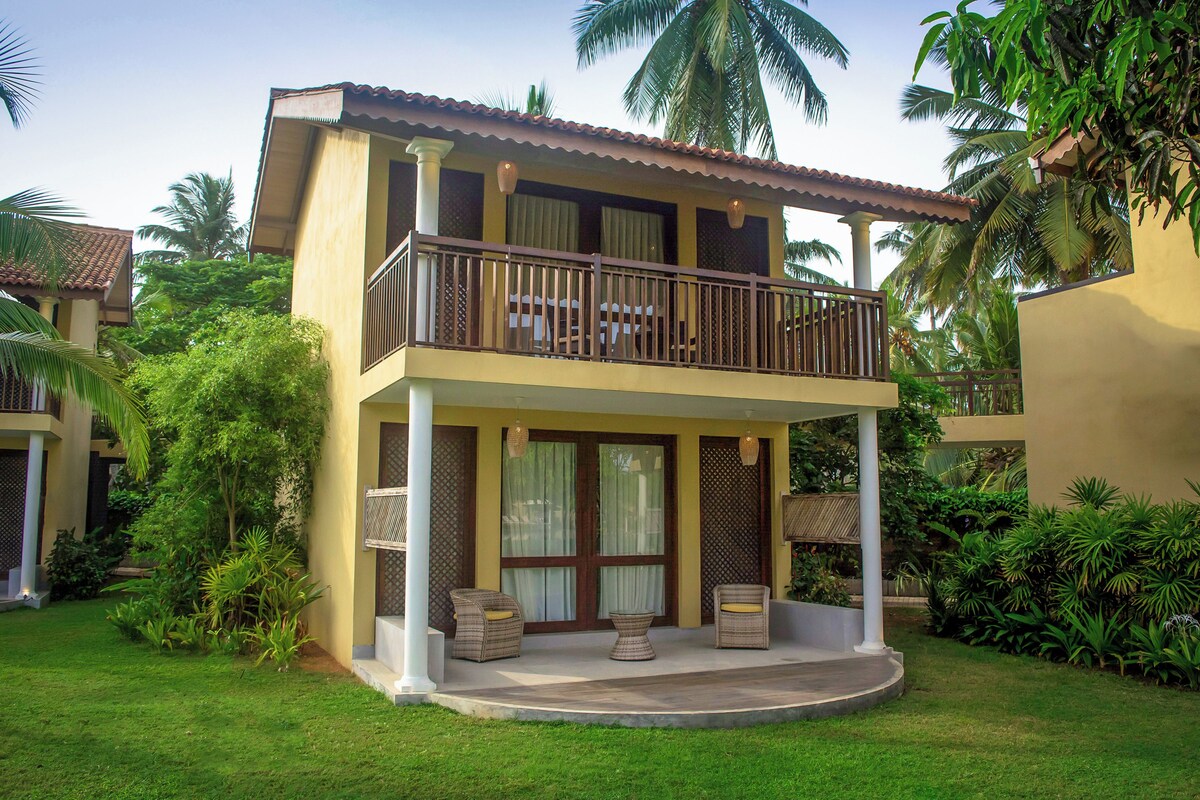 Un bâtiment à deux étages doté d’un balcon, entouré d’une végétation luxuriante et de palmiers.