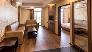 A modern hotel room with a sofa set, a flat-screen TV, a wooden cabinet, and a large mirror. - Le ROI Digha (Kanthi)