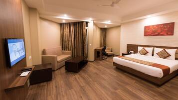 Una habitación de hotel con cama, sofá, escritorio con computadora, televisor y ventilador de techo.