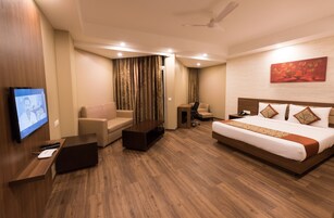 Una habitación de hotel con cama, sofá, escritorio con computadora, televisor y ventilador de techo.