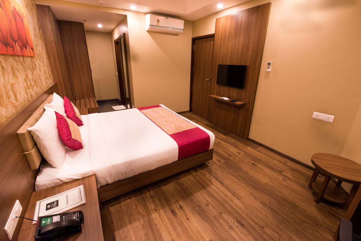 Une chambre d’hôtel avec un lit, une table de chevet avec un téléphone, un téléviseur fixé au mur et un plancher en bois.