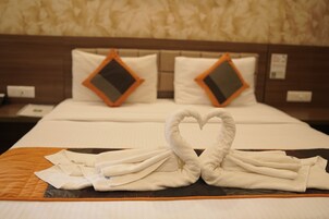 Habitación de hotel con una cama bien hecha, dos almohadas con fundas de forma de rombo y una toalla dispuesta en forma de corazón sobre la colcha.