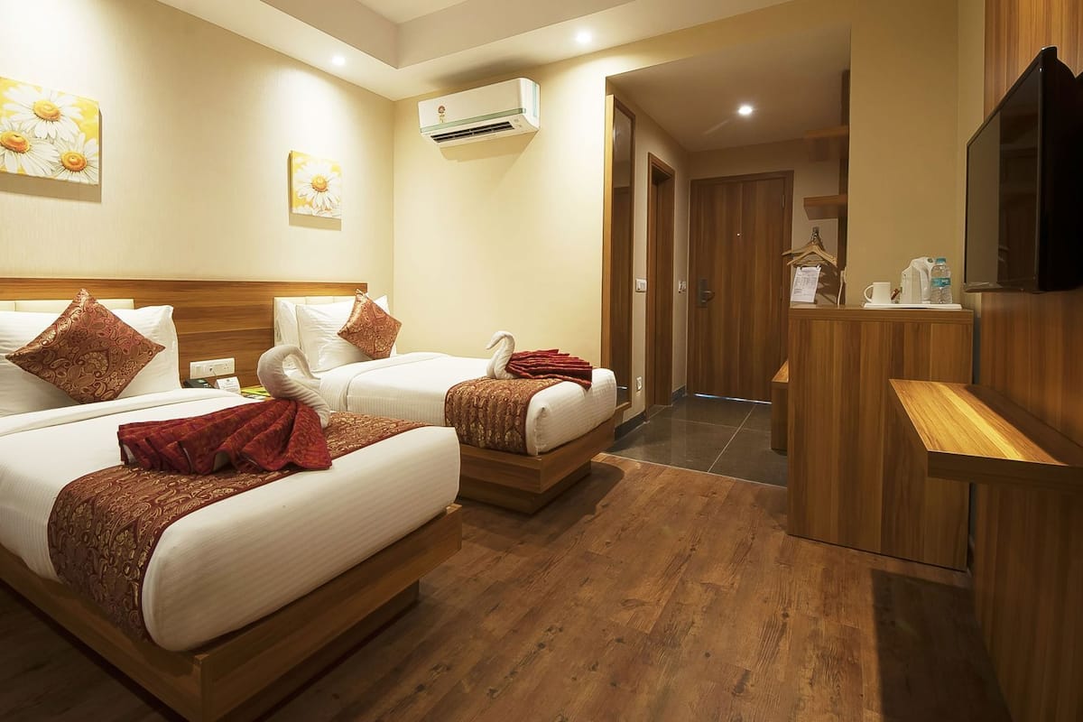 Une chambre d’hôtel avec deux lits, une tête de lit en bois, un téléviseur à écran plat, un bureau et un appareil de climatisation.