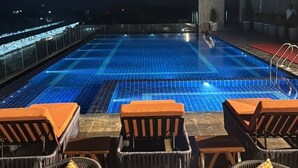 A rooftop pool area with lounge chairs and a view of the city at night. - Le ROI Digha (Kanthi)