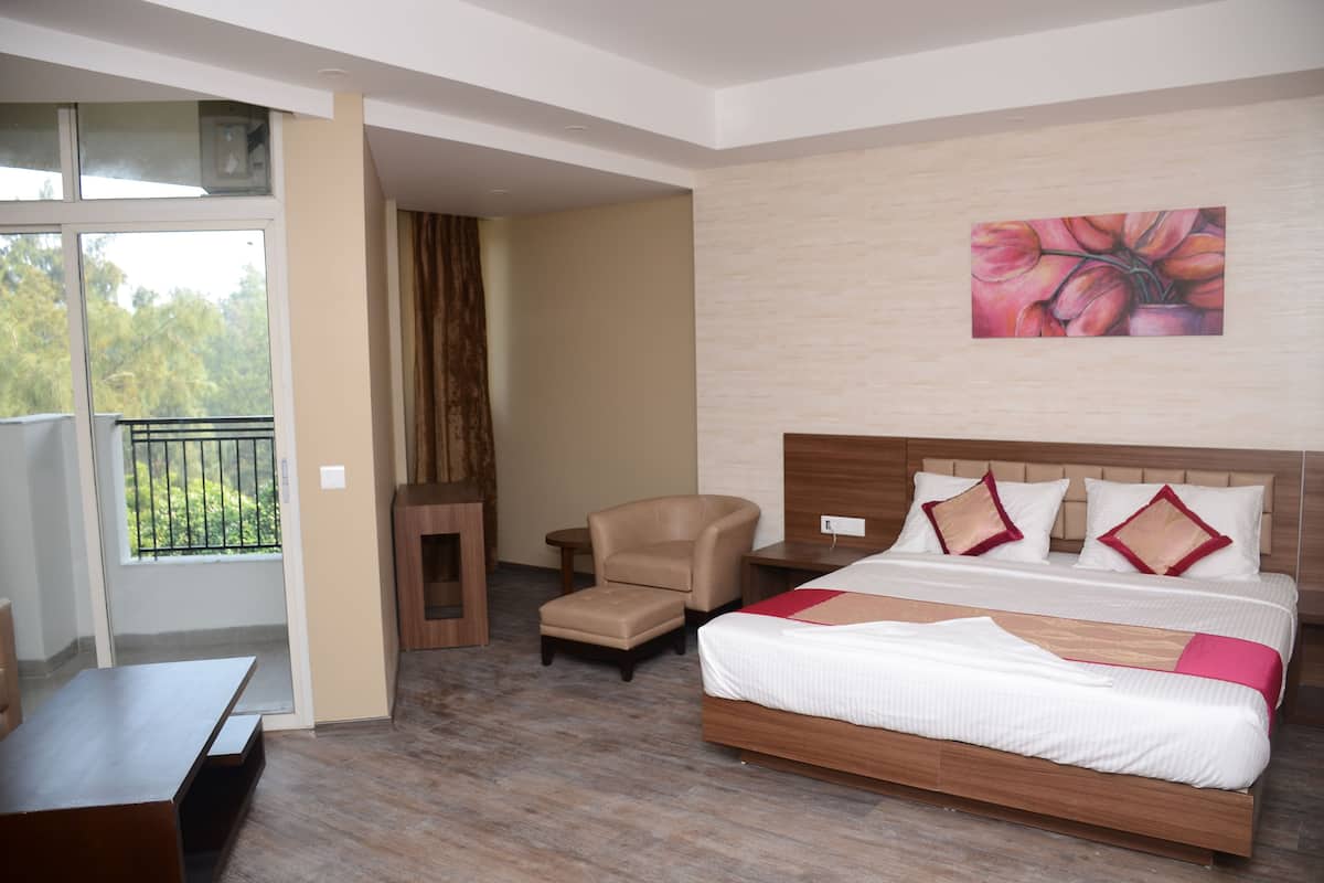 Une chambre d’hôtel avec un lit, une chaise, une petite table et un balcon donnant sur un paysage verdoyant.
