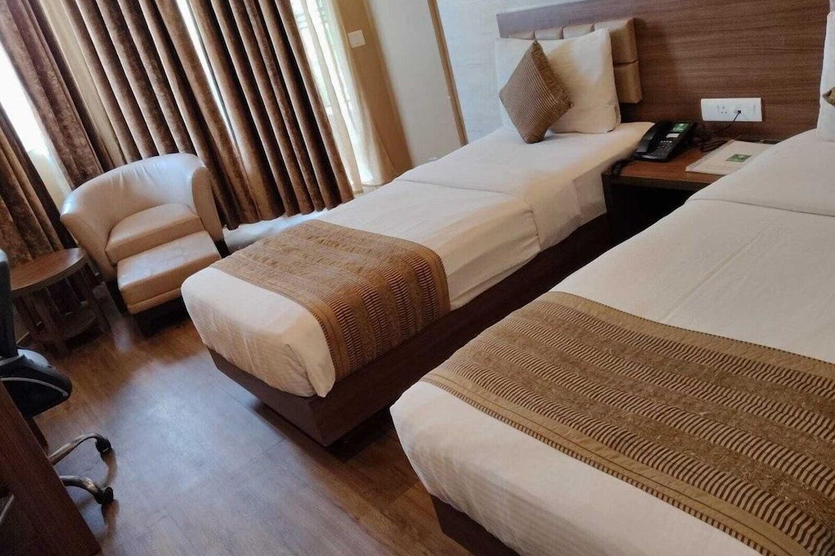 A hotel room with two beds, a chair, a bedside table with a phone, and a window with curtains.