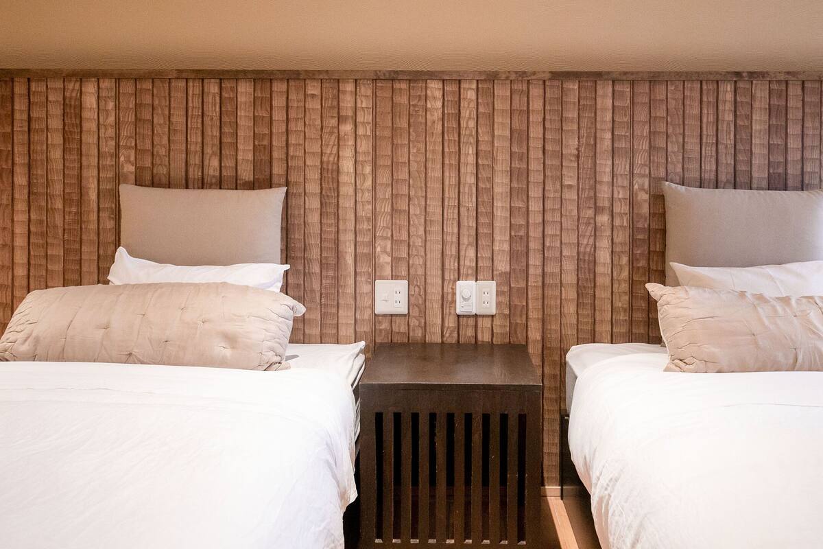 Une chambre d’hôtel avec deux lits simples, chacun doté d’un oreiller et d’une tête de lit en bois. Une petite table de chevet en bois se trouve entre les deux lits.