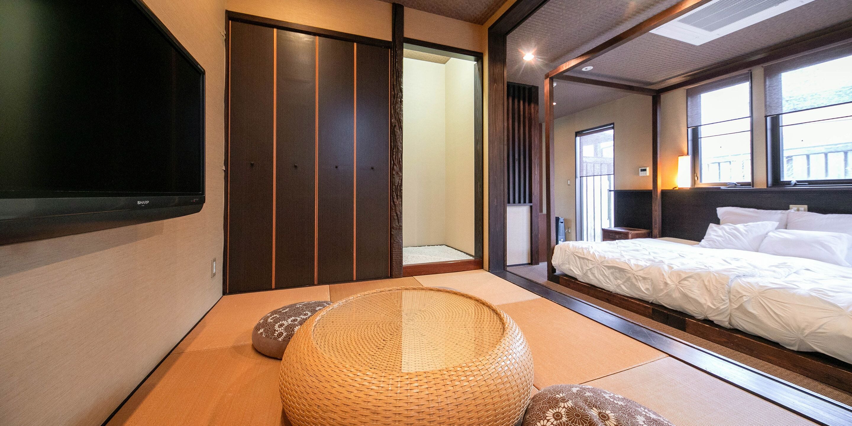 Quarto tradicional japonês com tatames, uma cama de madeira baixa e uma televisão na parede.