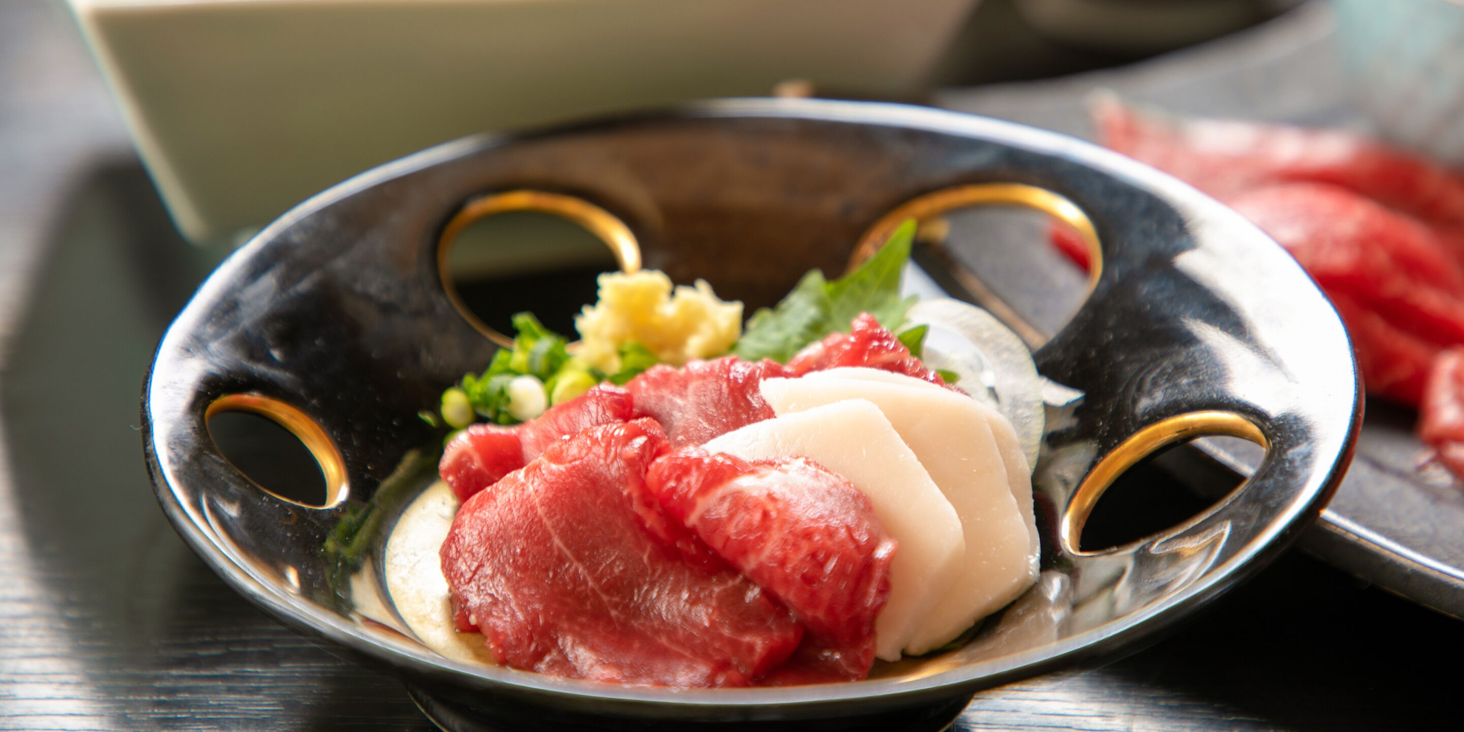 A metal plate with a hole in the center, containing sliced meat, a white item, and some green garnish.