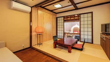 A traditional Japanese-style room with tatami flooring, a low wooden table, a cushioned bench, a tatami mat chair, a wooden cabinet, and a sliding shoji screen.