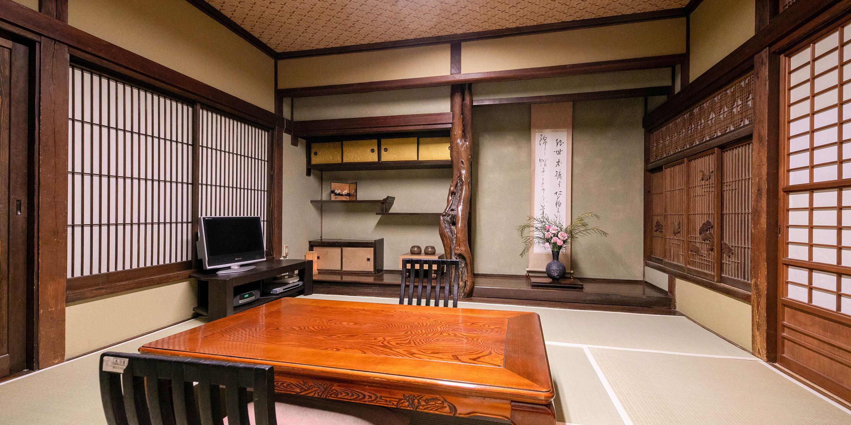 A traditional Japanese room with tatami flooring, a low wooden table, a television, and sliding doors with intricate designs.