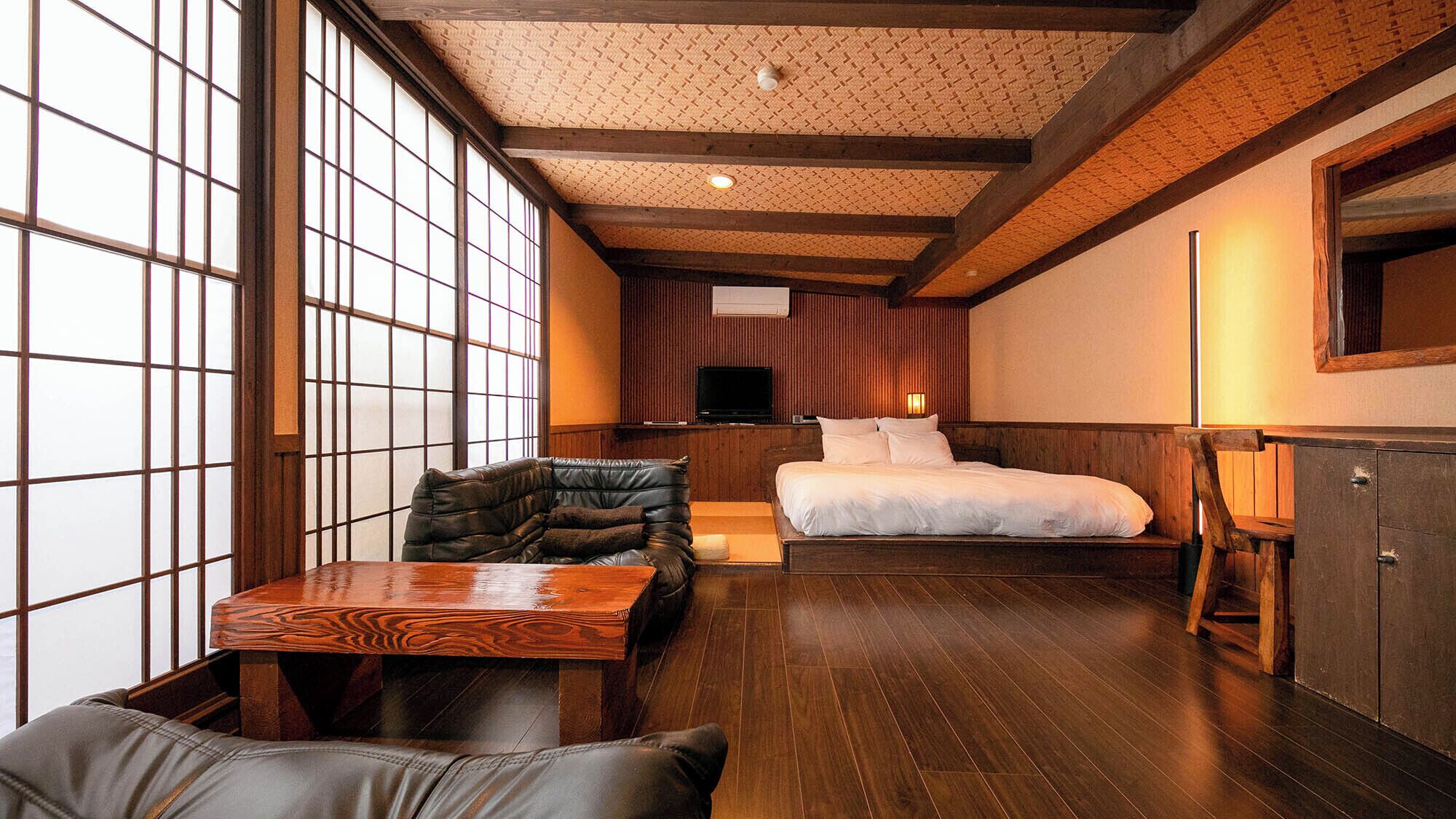 A traditional Japanese-style room with tatami flooring, a low wooden bed, a television, and a sliding door.