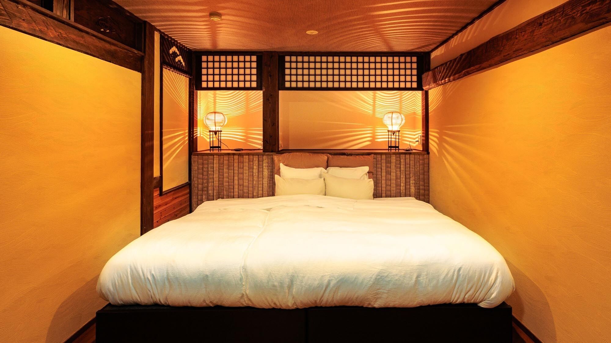 A traditional Japanese-style room with a wooden ceiling, a bed with white bedding, and two wall-mounted lamps.