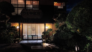 A traditional Japanese building at night with a signboard, illuminated entrance, and surrounding greenery. - Tsuruya (Aso)