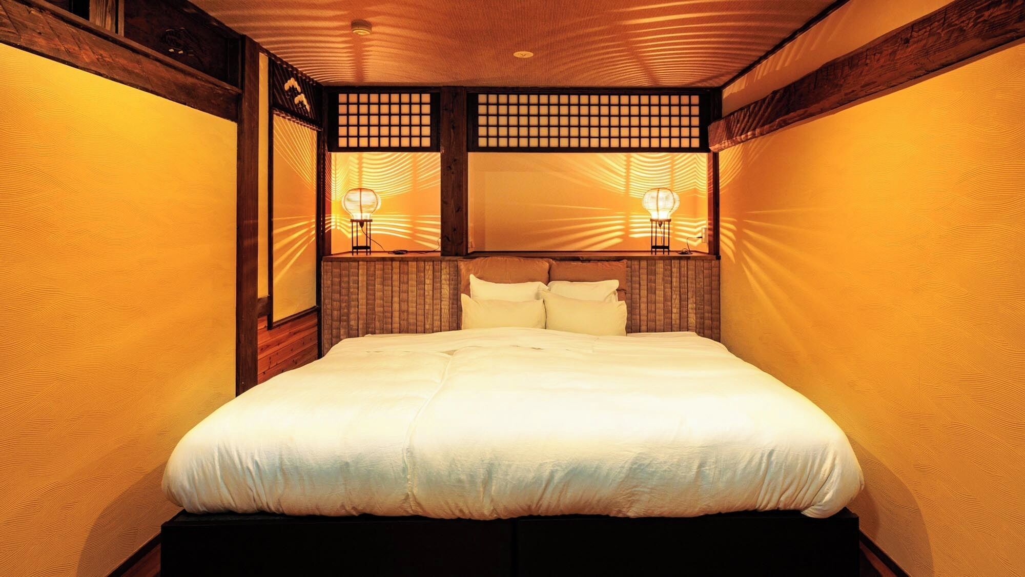 A hotel room with a large bed, wooden headboard, and two wall-mounted lamps.