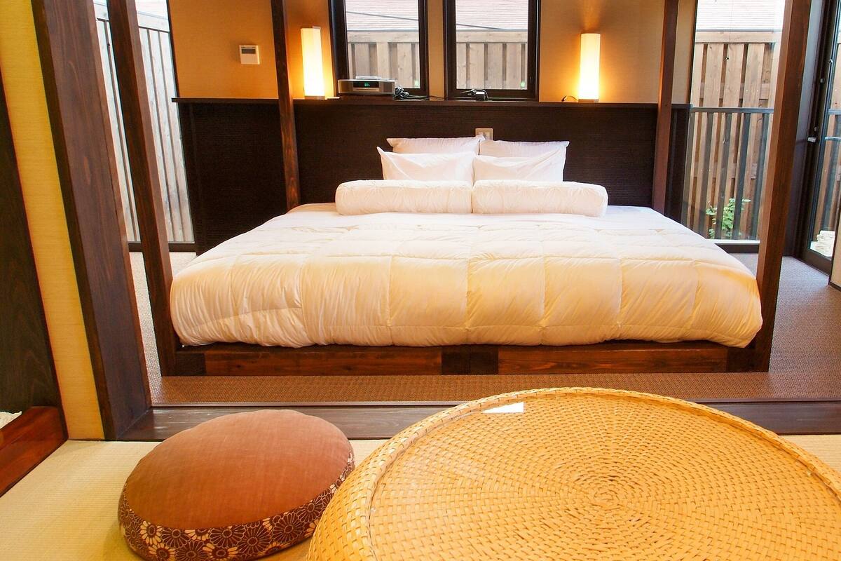 Une chambre d’hôtel avec un grand lit, une tête de lit en bois, un balcon avec vue et un tapis traditionnel tissé.