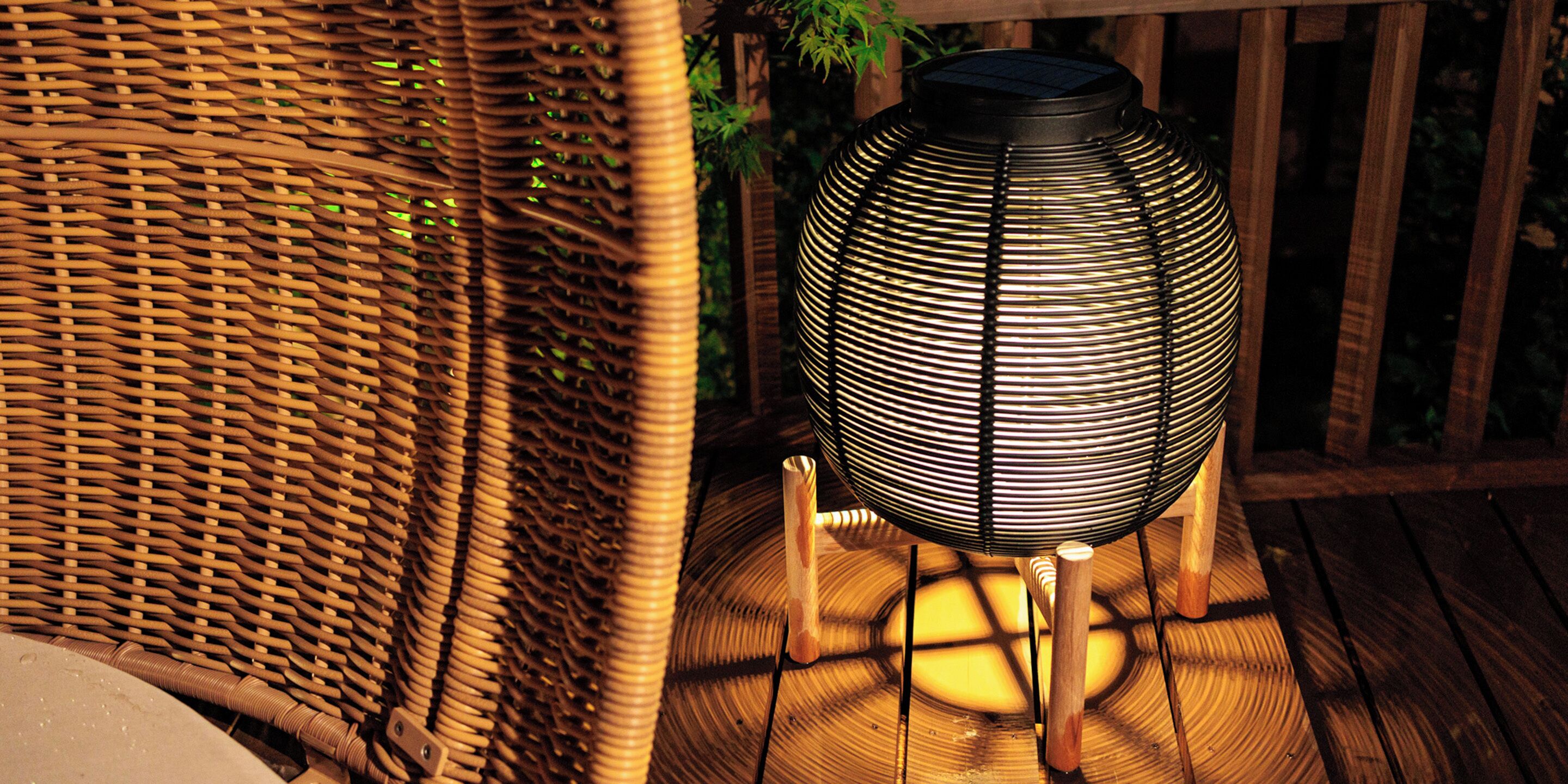 A wicker chair and a spherical, ribbed outdoor lamp on a wooden deck.
