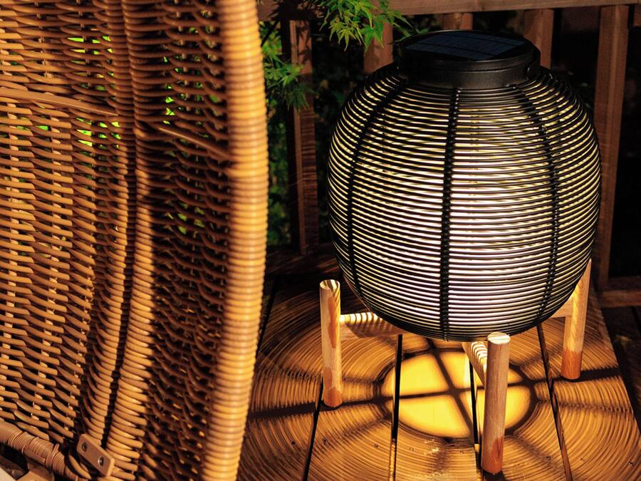 A wicker chair and a spherical, ribbed outdoor lamp on a wooden deck.