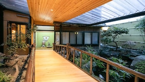 A wooden deck leading to a traditional Japanese building with a green door and sliding doors. - Tsuruya (Aso)
