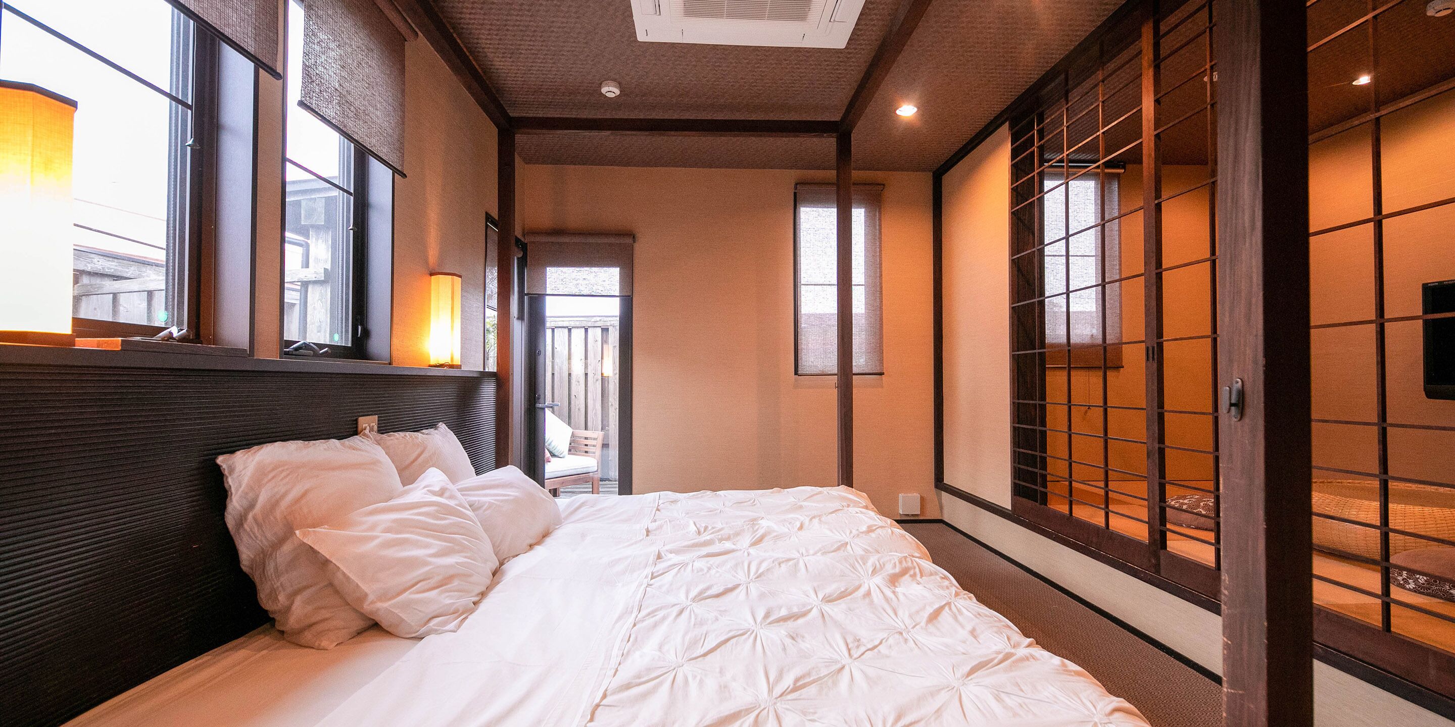Quarto de hotel com cama grande, cabeceira de madeira e portas deslizantes com padrão de grade.