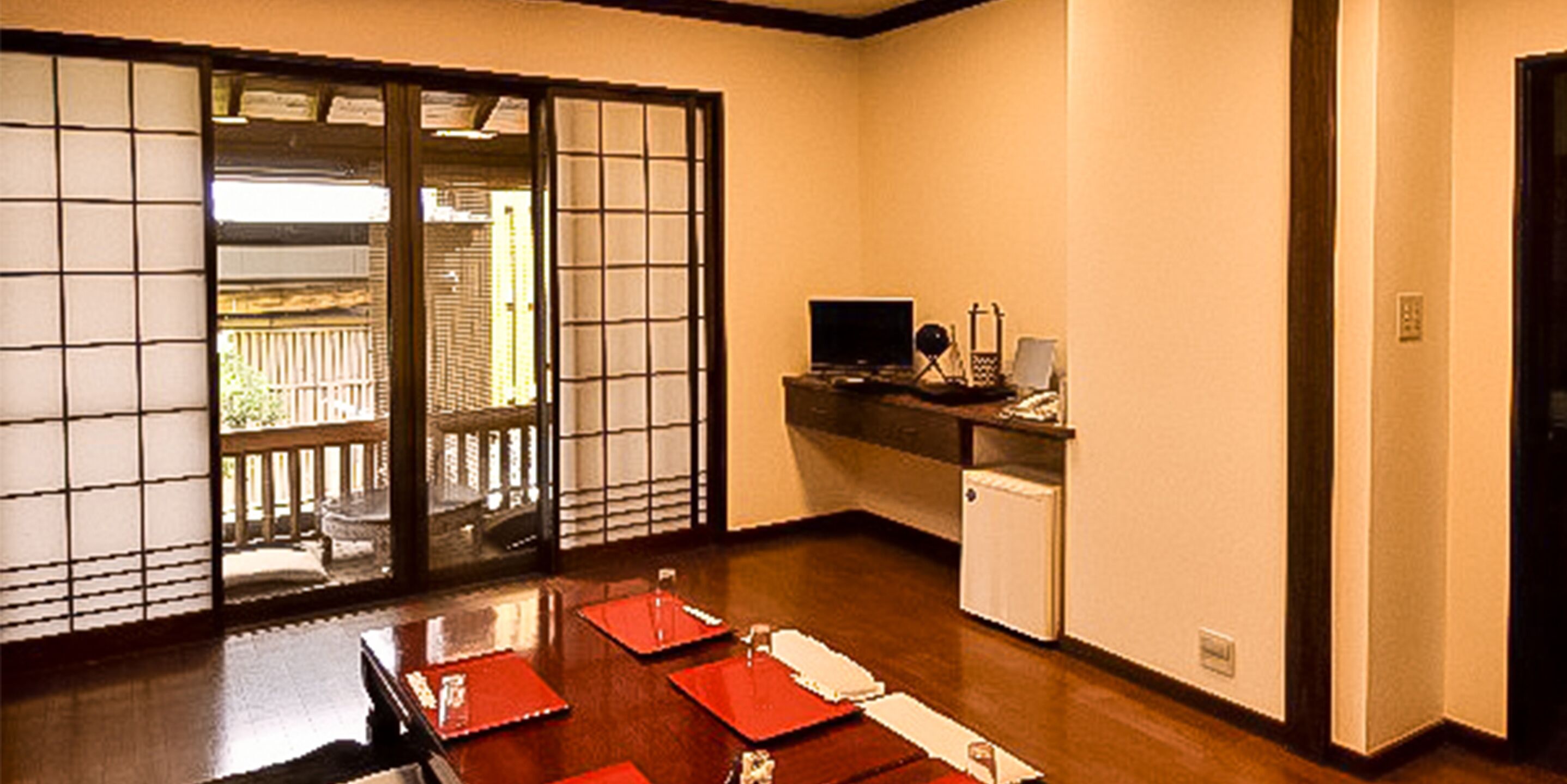 A traditional Japanese room with tatami flooring, a sliding door, a small desk with a computer, and a view through the door.