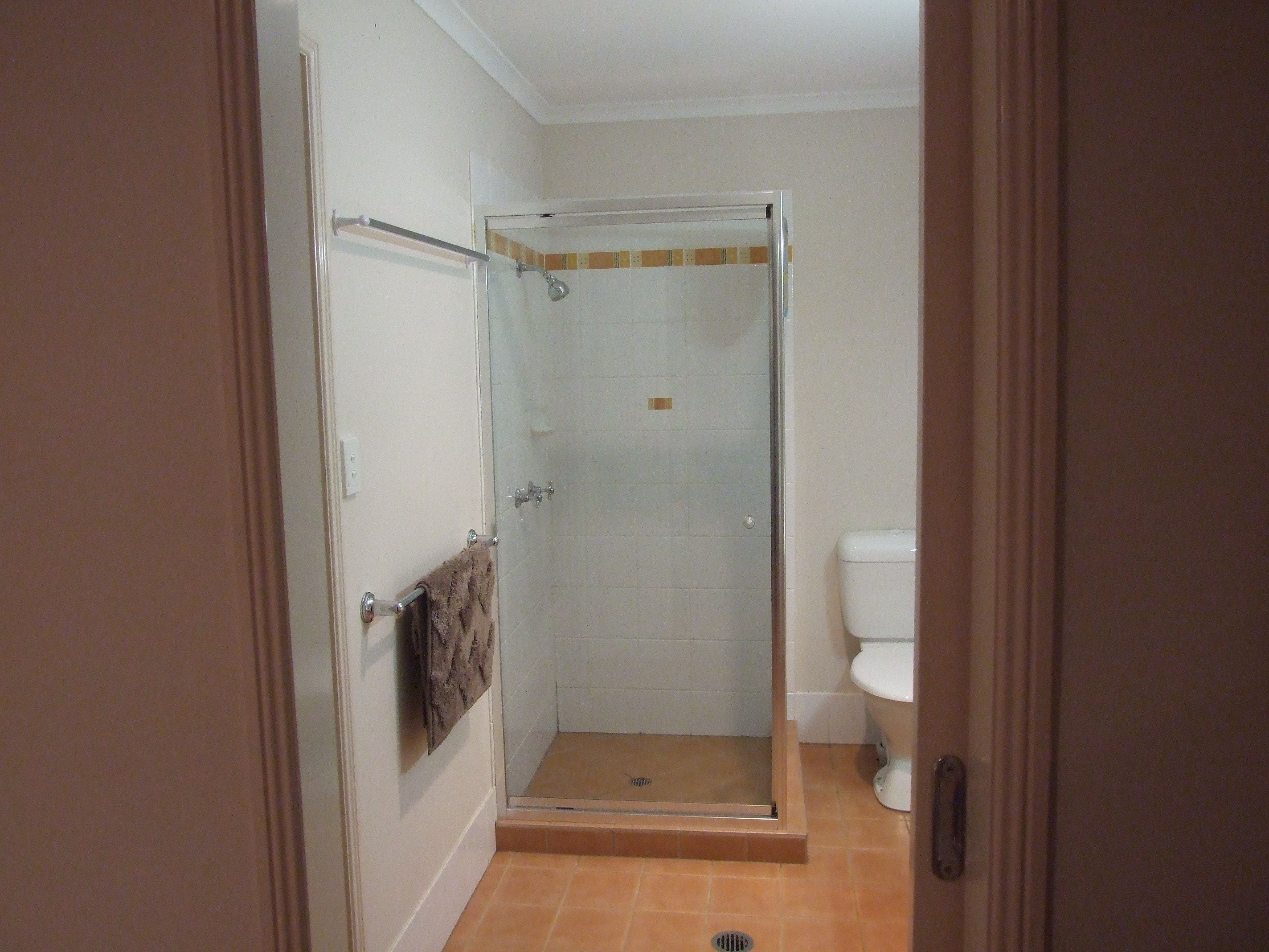 Un petit espace douche fermé, doté d’une porte en verre, une serviette accrochée à la poignée de la porte, et des toilettes visibles sur la droite.