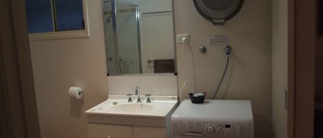 A compact bathroom with a sink, mirror, and a front-loading washing machine.