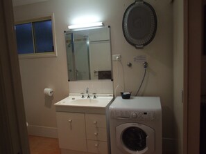 A compact bathroom with a sink, mirror, and a front-loading washing machine. - Lake Barra Cottages (Anderleigh)