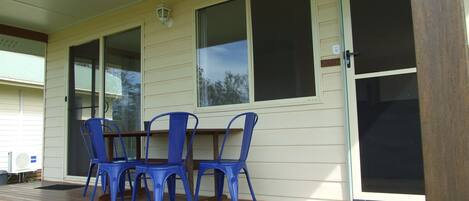 Un espacio exterior techado con una mesa y sillas azules, ventanas amplias y una puerta corrediza de vidrio.