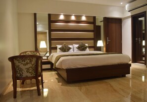 Una habitación de hotel con una cama grande, una mesita de noche, dos sillas, un espejo y un armario.