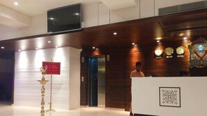 A hotel reception area with a modern design, a reception desk, a digital screen, and a clock on the wall. - South Coast Hotels Thane (Thane)