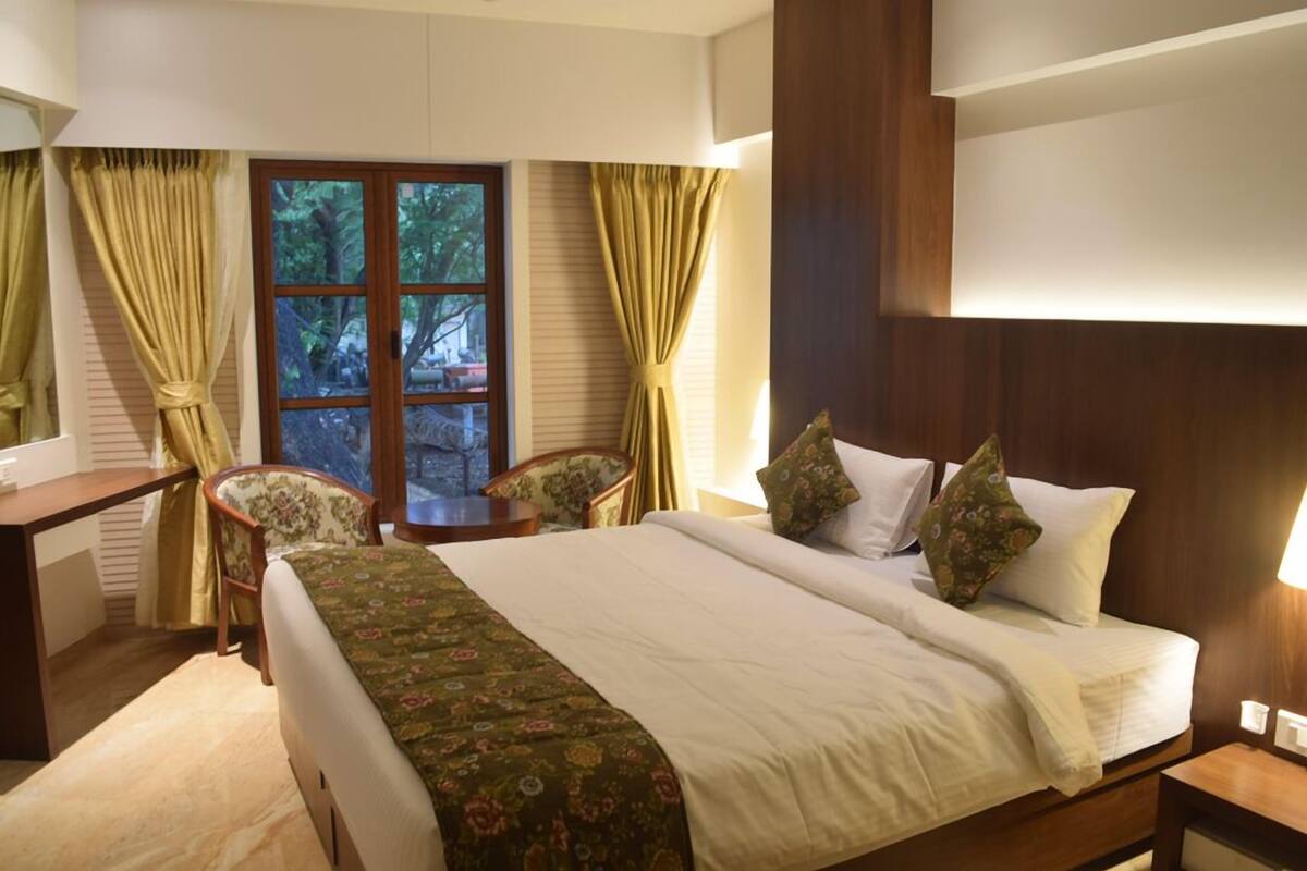 A hotel room with a bed, a desk, a chair, and a window with curtains.