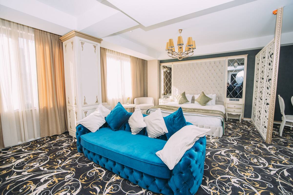 Ein Hotelzimmer mit einem blauen Sofa, einem weißen Bett und einem gemusterten Teppich.