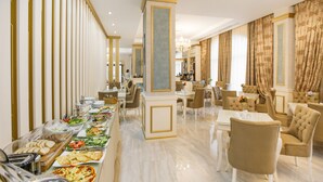 Un área de bufé con diversas opciones de comida, un espacio de estar con sillas y mesas, y una columna decorativa en el centro.