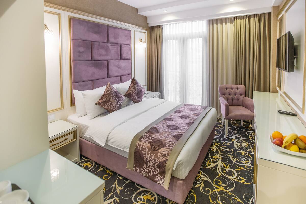 Ein Hotelzimmer mit einem großen Bett, einem Sessel, einem Fernseher und einer Obstschale.