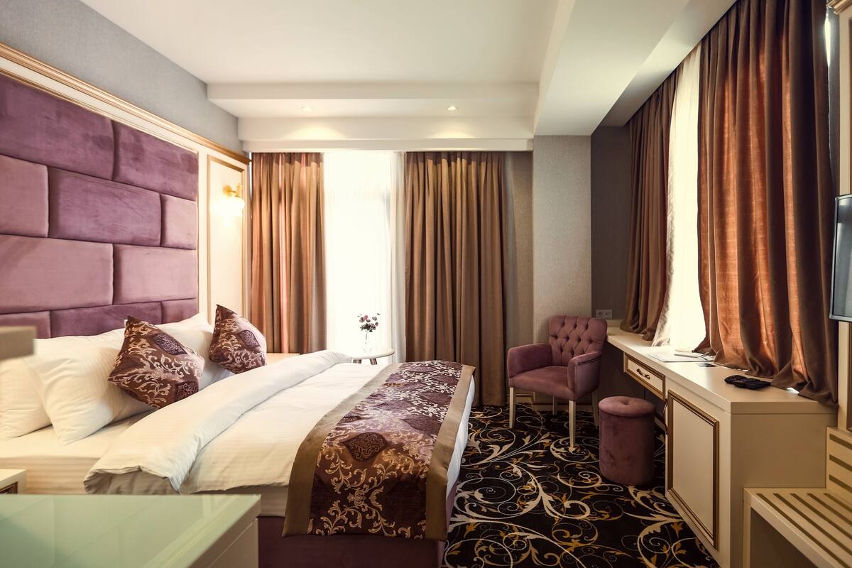 Ein Hotelzimmer mit einem großen Bett, einem Schreibtisch, einem Sessel und einem Fernseher.