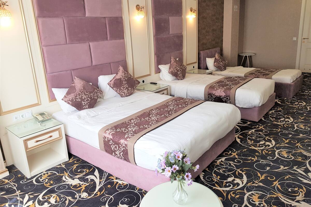 Ein Hotelzimmer mit einem großen Bett, einem kleineren Bett, einem Nachttisch mit Telefon und einer dekorativen Vase mit Blumen.