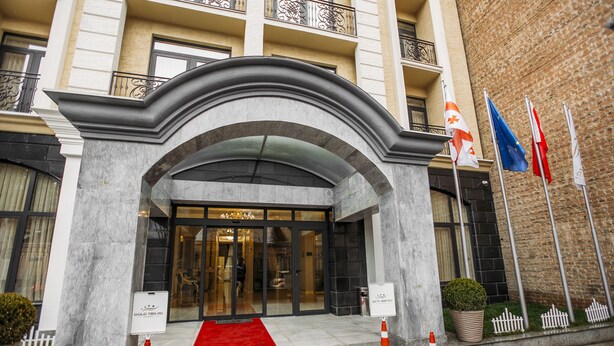 Entrada de hotel con alfombra roja, un cartel y banderas.