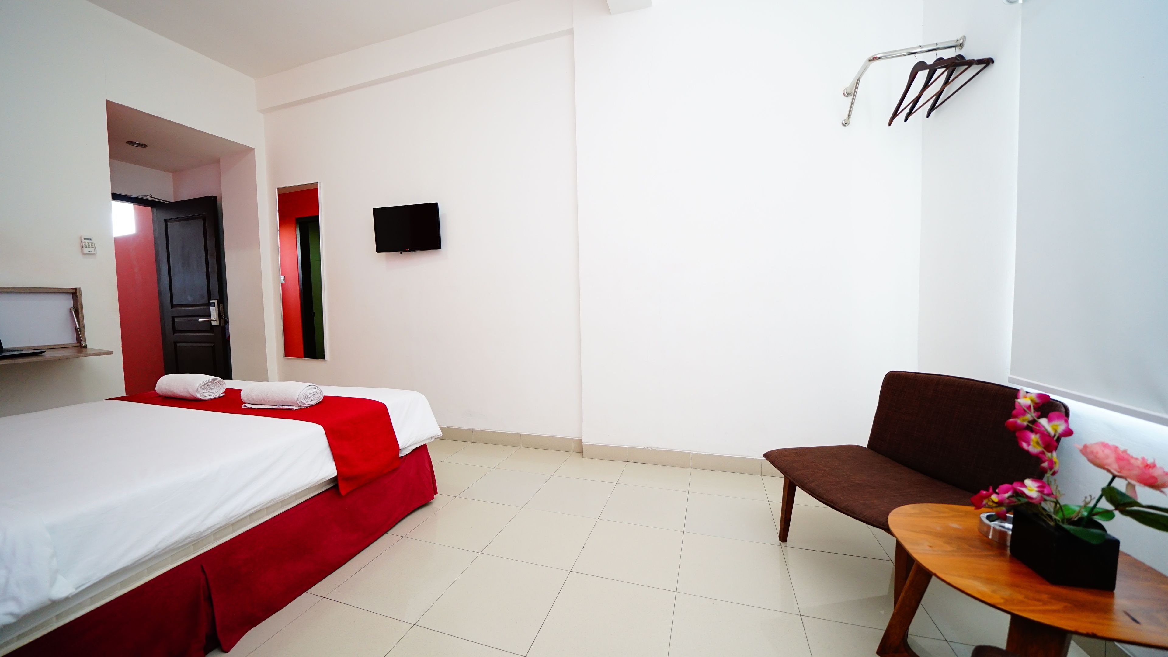Une chambre d’hôtel avec un lit, une chaise, une petite table sur laquelle se trouve un vase, un téléviseur et une porte dont le cadre est rouge.