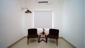 A small, clean room with two dark brown chairs, a small round table, and a potted plant. - Amaia Hotel (Mataram)