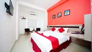 A hotel room with a bed, a desk, a chair, a TV, and a wall with pictures. - Amaia Hotel (Mataram)