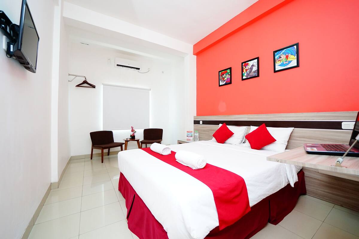 A hotel room with a bed, a desk, a chair, a TV, and a wall with pictures.