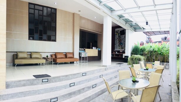 A modern lobby with a reception desk, a sofa, and a staircase leading to outdoor seating. - Amaia Hotel (Mataram)