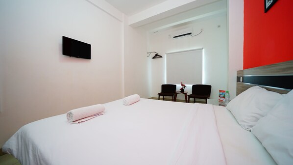 A hotel room with a bed, a TV, a mirror, a chair, and a small table. - Amaia Hotel (Mataram)