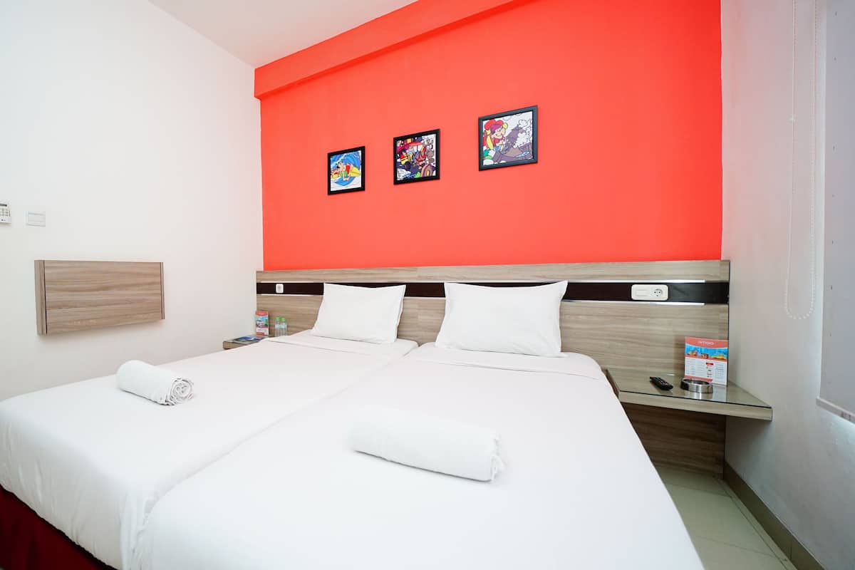 A hotel room with a large bed, white bedding, a red accent wall, and three framed pictures.